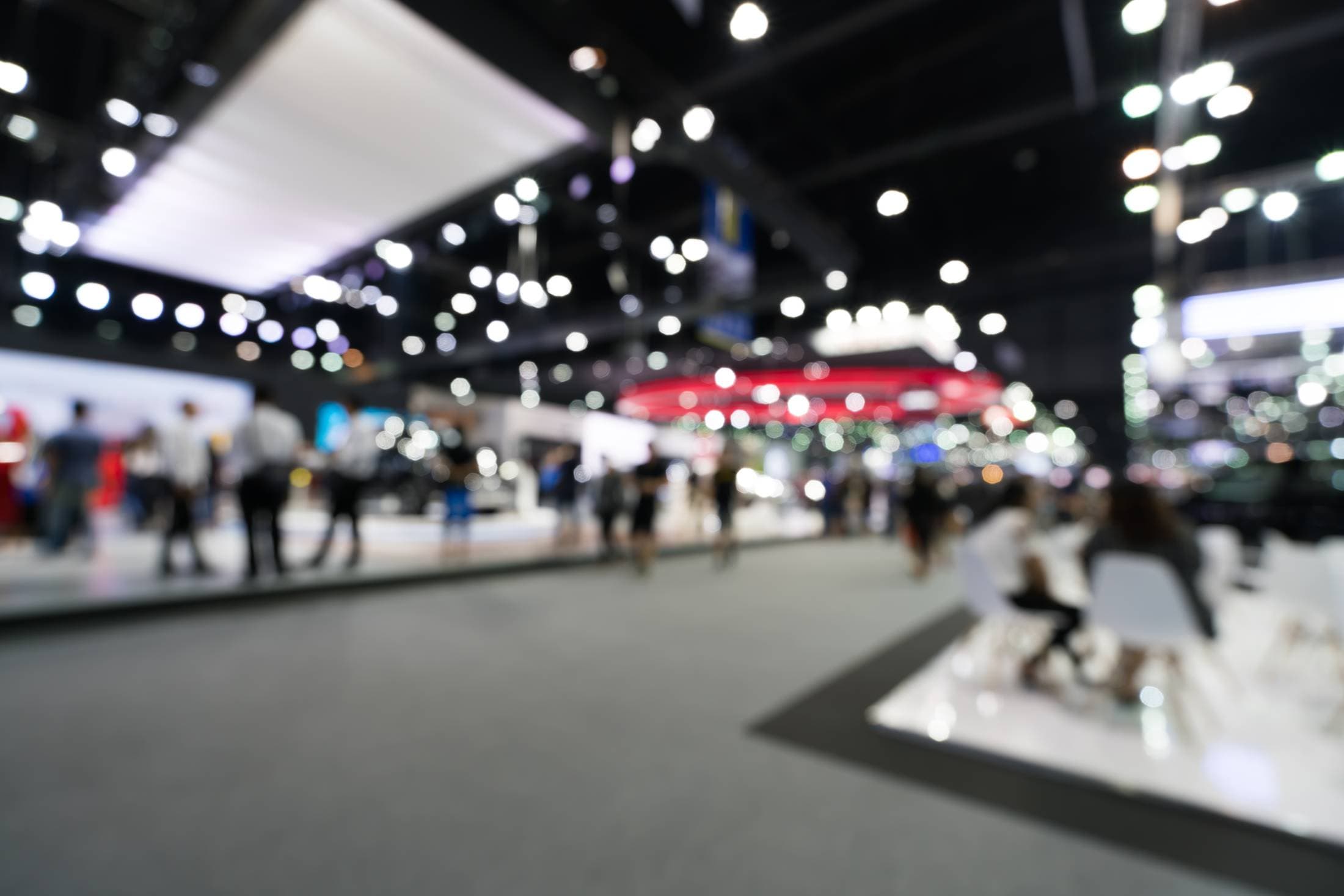 A bright, crowded car show hall, out of focus