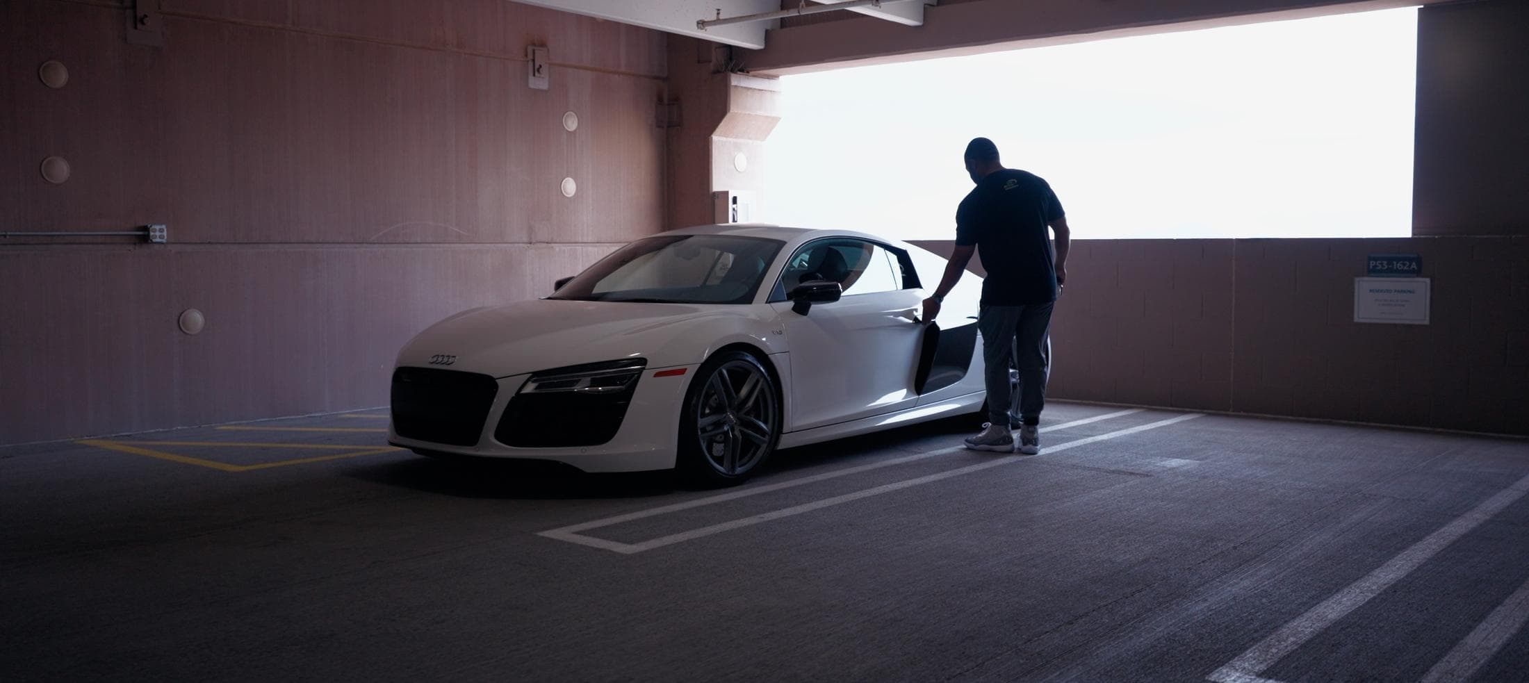 A white Audi R8 in a parking garage with a man opening its door