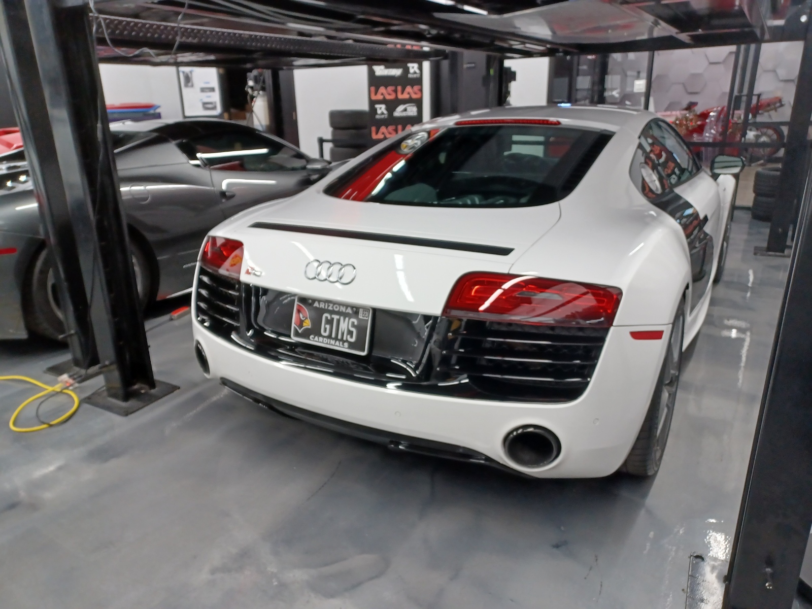 White Audi R8 V10 rear 3/4 inside a lift shop, epoxy floor, LAS branding on wall