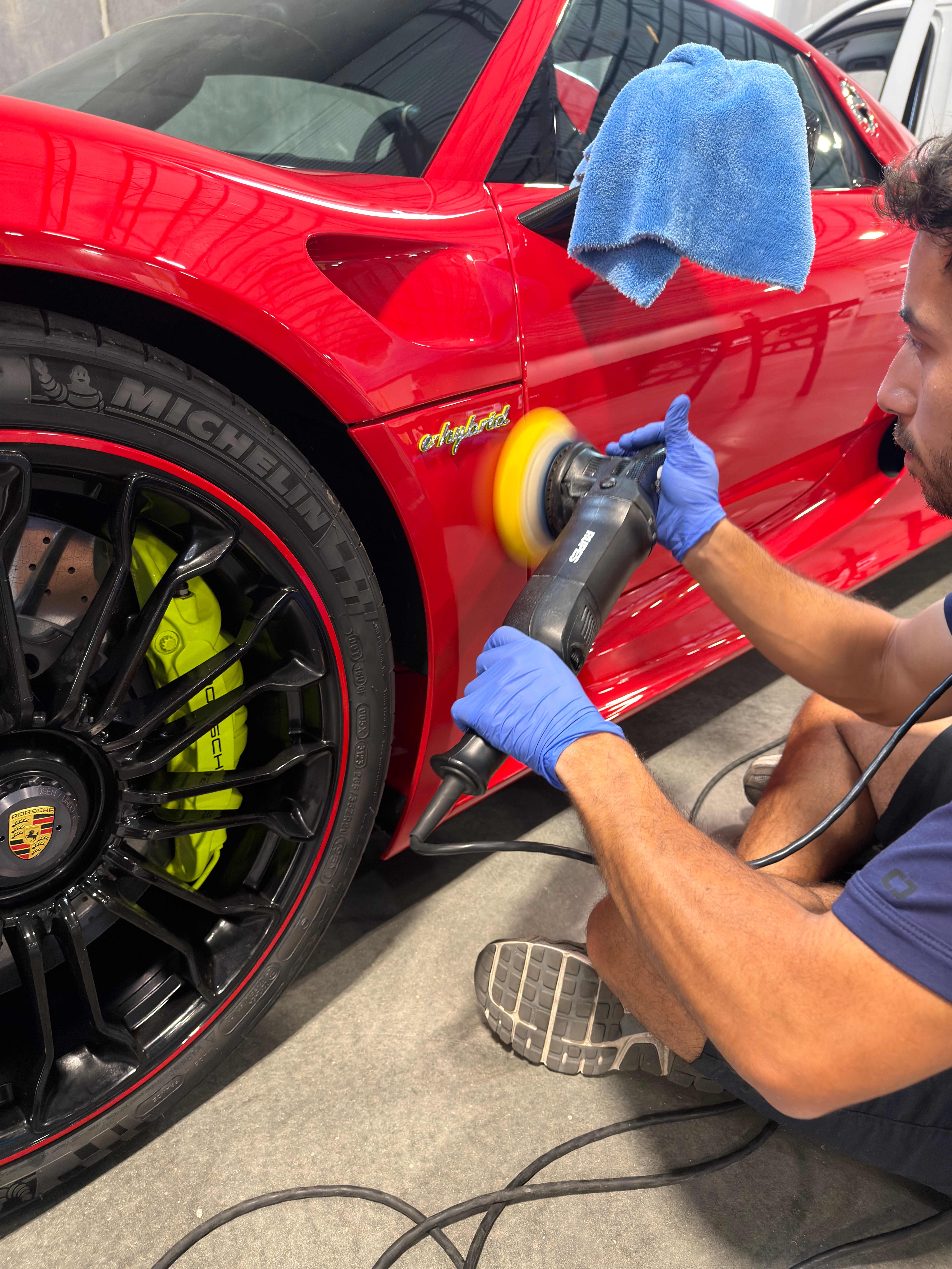Porsche 918 Spyder Guards Red paint correction, technician polishing lower rocker with DA polisher, neon yellow calipers visible