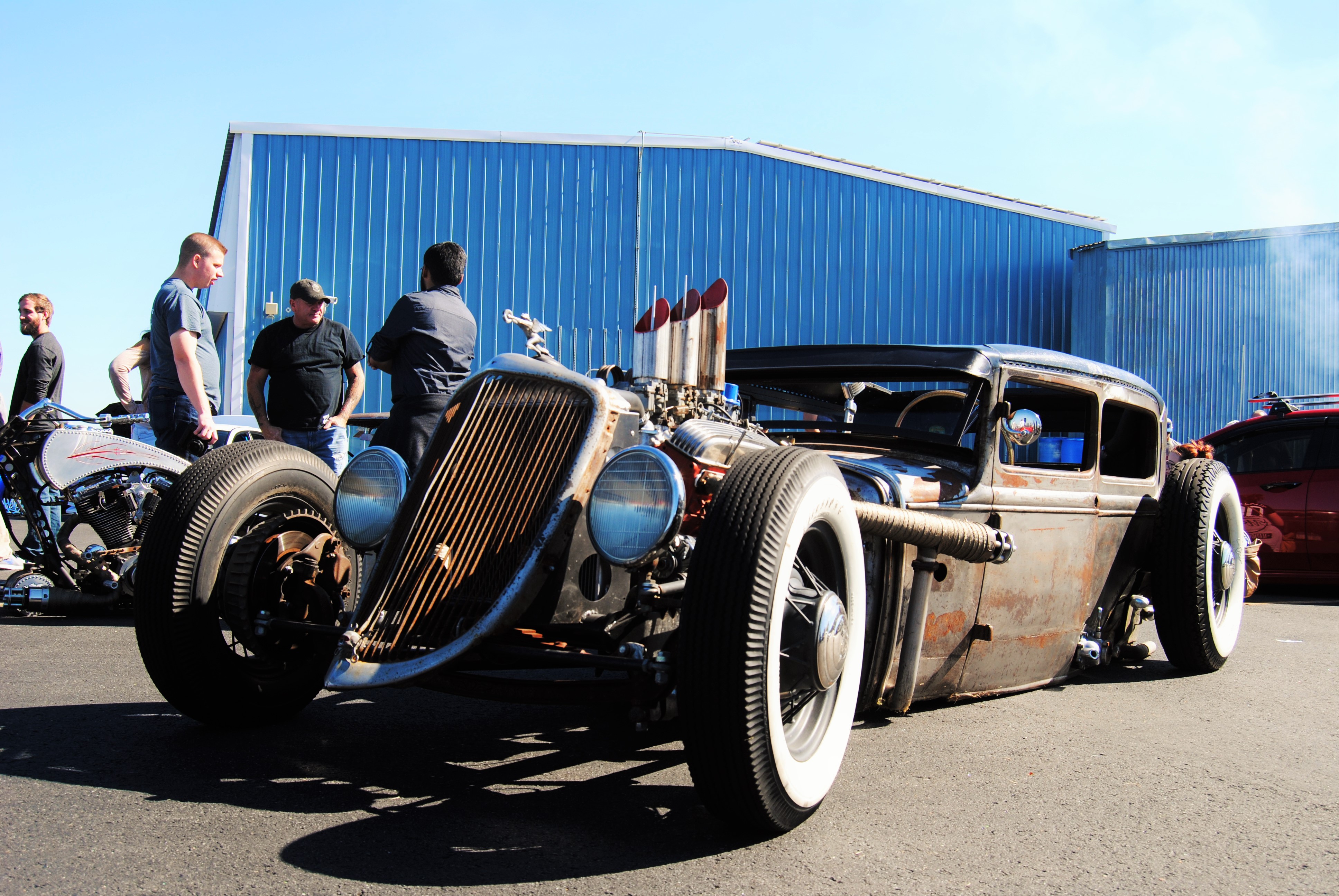 Vintage rat rod with patina steel, whitewall tires, exposed engine with exhaust stacks at car show